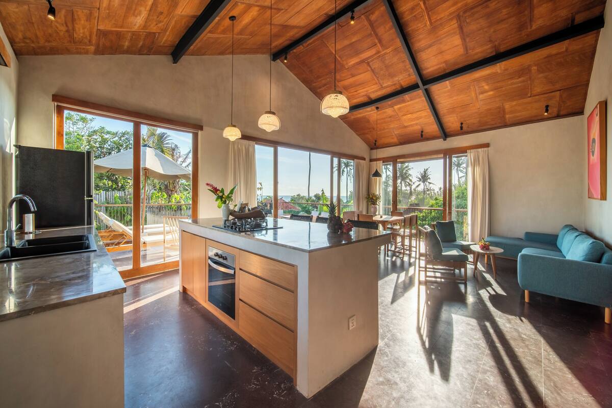 A spacious kitchen with a central island, large windows, and a high ceiling with exposed beams.