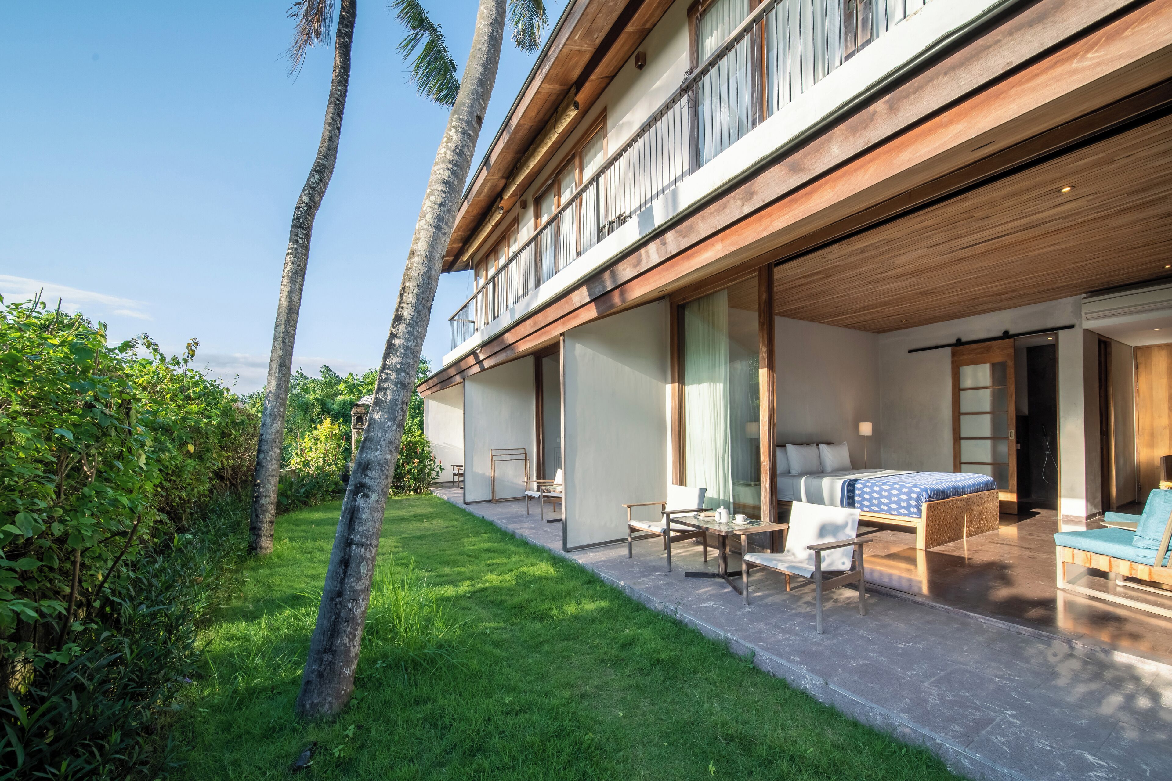 A modern building with a covered outdoor area featuring a bed, chairs, and a table.