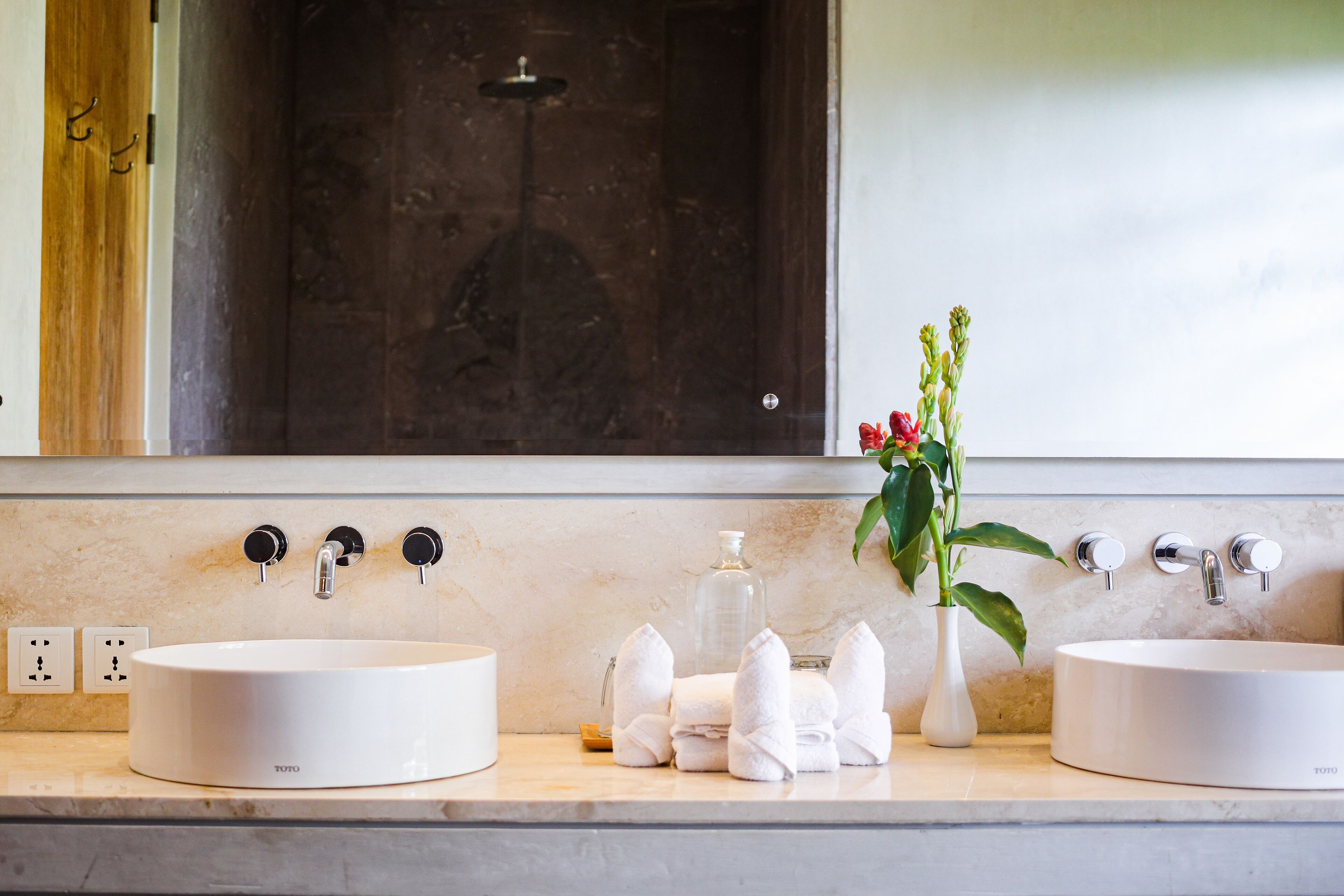 Un baño con dos lavamanos, un espejo y una ducha. Hay toallas y un florero con flores en la encimera.
