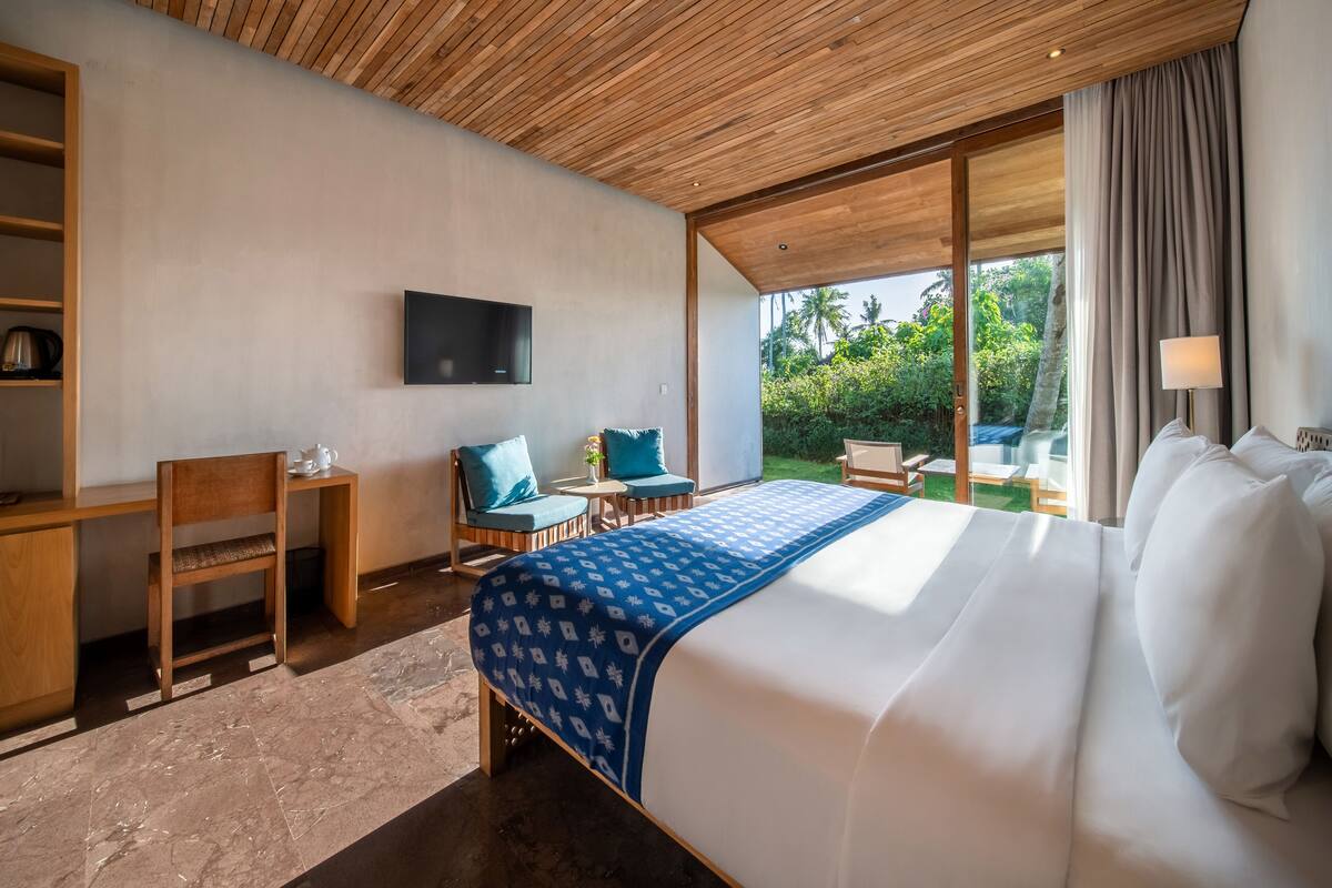 A modern hotel room with a large bed, a desk, a chair, and a TV.