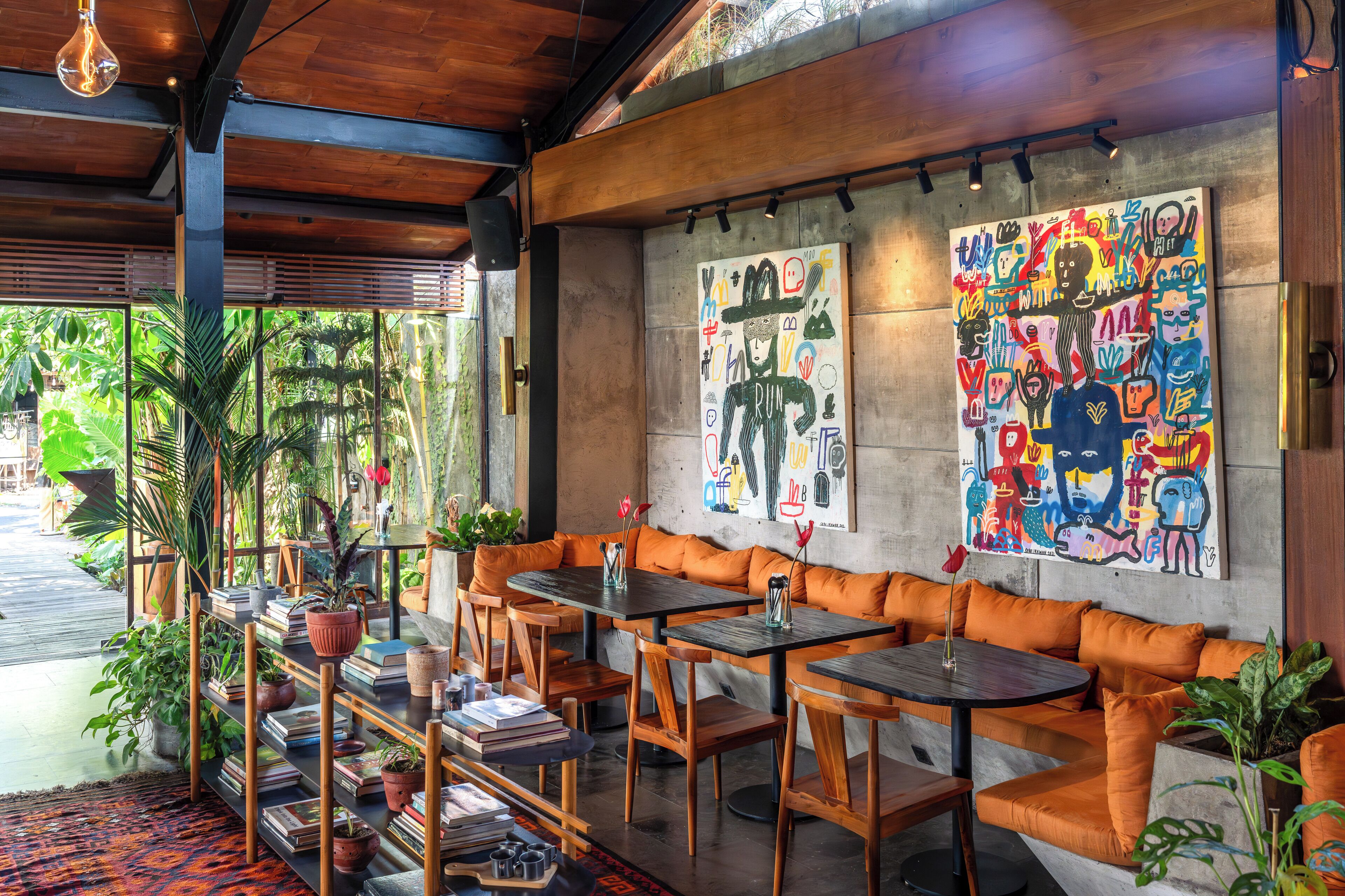 A cozy cafe with wooden furniture, a bookshelf, and vibrant artwork on the walls.