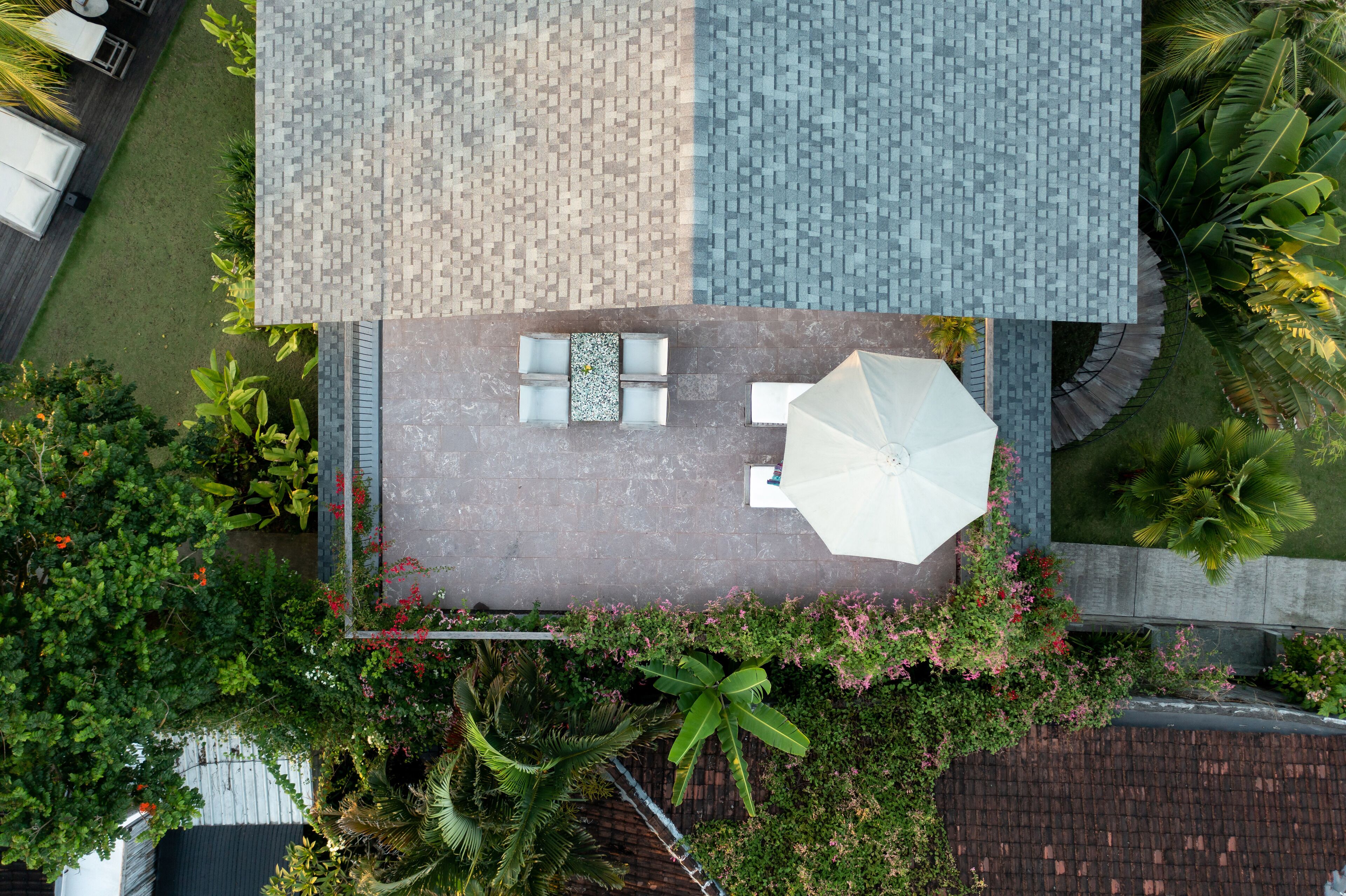 Vue aérienne d’une terrasse sur le toit, avec un espace salon, un parasol blanc et de la verdure environnante.