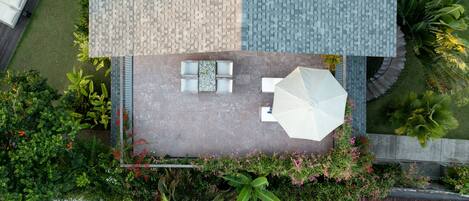 Vue aérienne d’une terrasse sur le toit, avec un espace salon, un parasol blanc et de la verdure environnante.