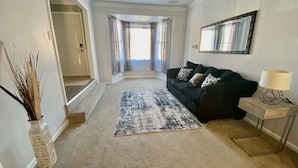 A living room with a dark green sofa, a patterned rug, a vase with dried plants, and a lamp on a side table. - Super Nice townhouse in Virginia Beach (Virginia Beach)