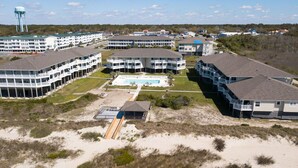 Un hôtel situé sur la côte, composé de plusieurs bâtiments, doté d’une piscine centrale et d’une plage de sable.