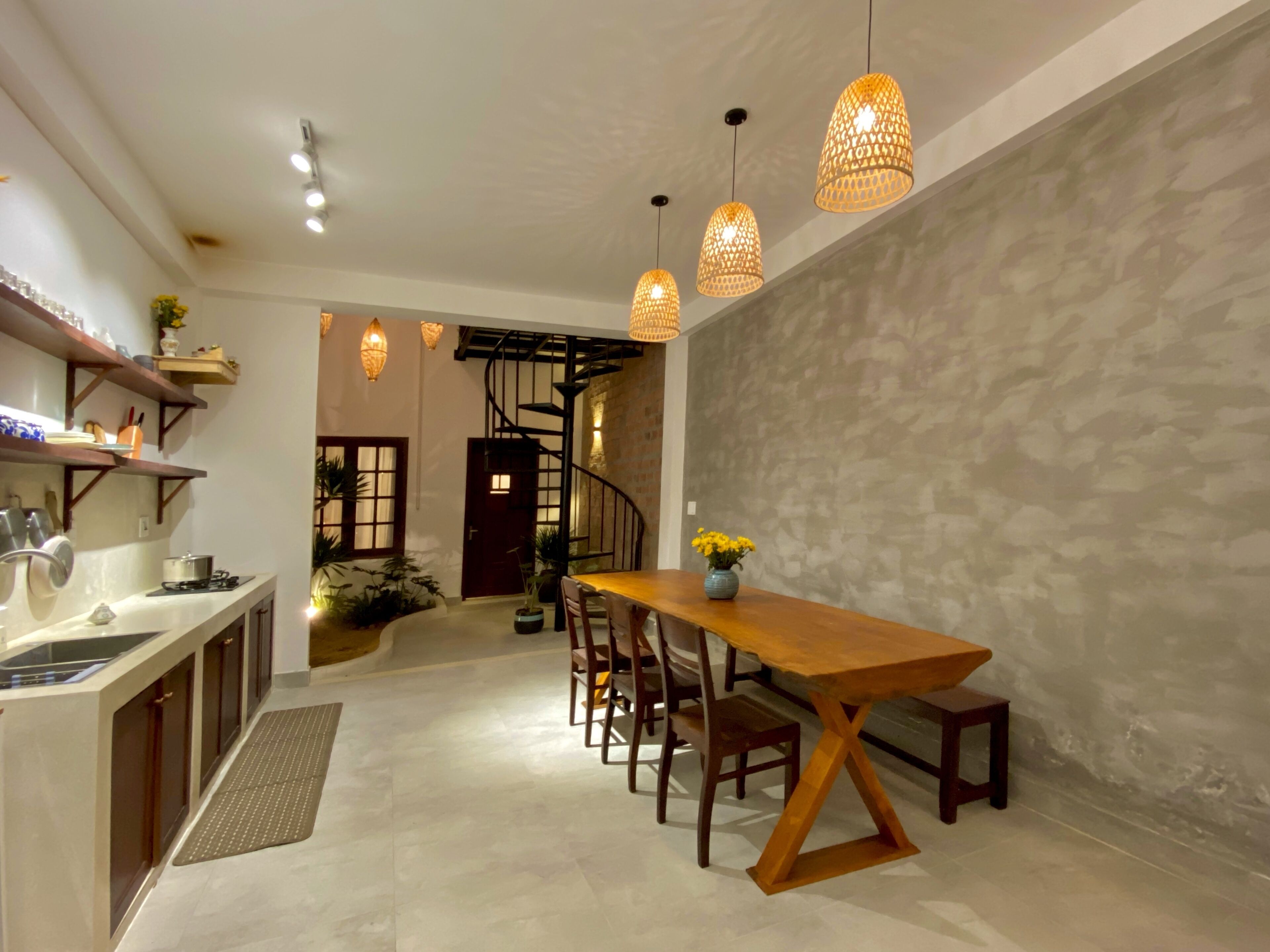 A modern kitchen with a wooden dining table, pendant lights, and a staircase leading to another level.