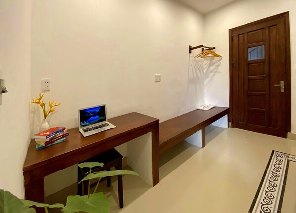 A hallway with a wooden bench, a laptop, a vase with yellow flowers, and a door.