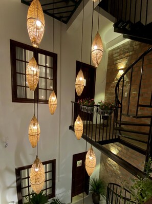 Ein mehrgeschossiges Interieur mit hängenden Korbschwingenlüstern, einer Backsteinwand und einer Treppe.