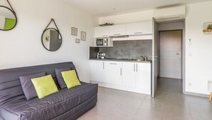 A modern living room with a grey sofa and a kitchen area with white cabinets and a microwave. - Studio Aloe - Welkeys (Cavalaire-sur-Mer)