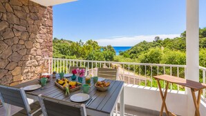 Un balcon avec un mur en pierre, une table dressée pour le petit-déjeuner et une vue sur la mer.