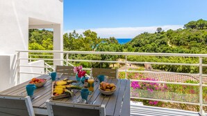 A balcony with a table set for breakfast, overlooking a lush landscape and the sea.
