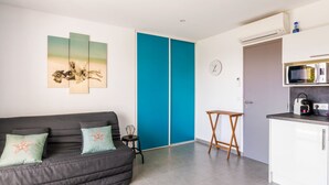A modern living room with a grey sofa, teal cushions, a blue partition, a small wooden table, and a kitchenette with a microwave.