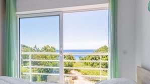 Una habitación con un gran ventanal corredero que da a un balcón con vistas al mar y al verdor.