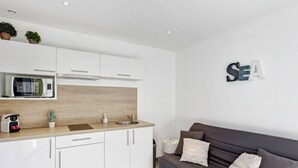 Una cocina moderna con armarios blancos, encimera de madera y microondas integrado. Hay un sofá oscuro con cojines y un letrero en la pared que dice "SEA".