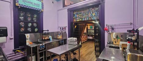 A kitchen area with stainless steel appliances, a coffee machine, and a variety of kitchen utensils. There is a sign above the counter that reads "gaslamp hostel SAN DIEGO".