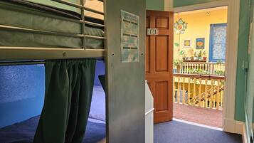 A bunk bed room with a wooden door leading to a balcony with a railing and potted plants.