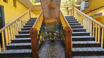 A staircase with blue carpeted steps and wooden balusters, leading to a balcony with yellow walls and a view of the sky.