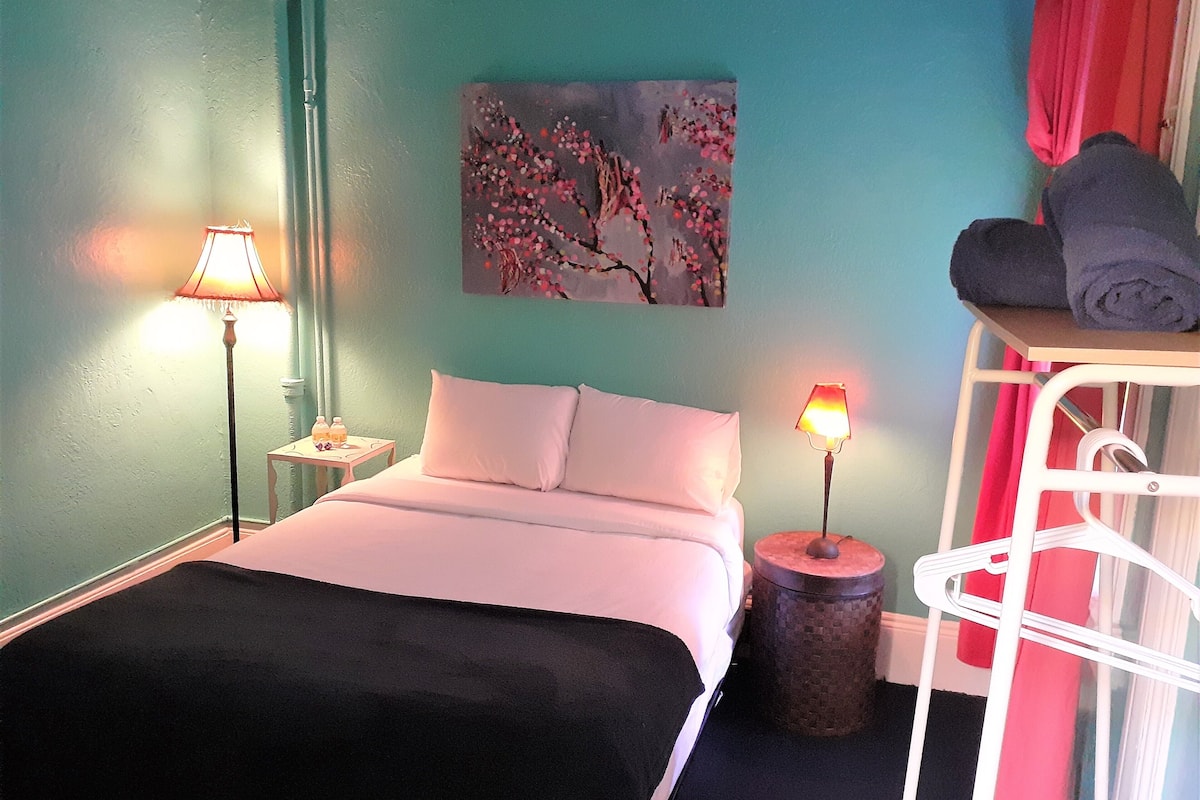 Une chambre à coucher avec un lit, deux tables de chevet avec des lampes, un tableau au mur et une étagère avec des serviettes.