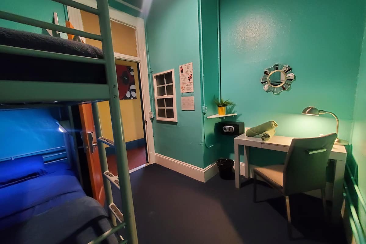 Une chambre avec un lit superposé, un bureau et une chaise, une petite étagère avec une plante et une horloge murale.