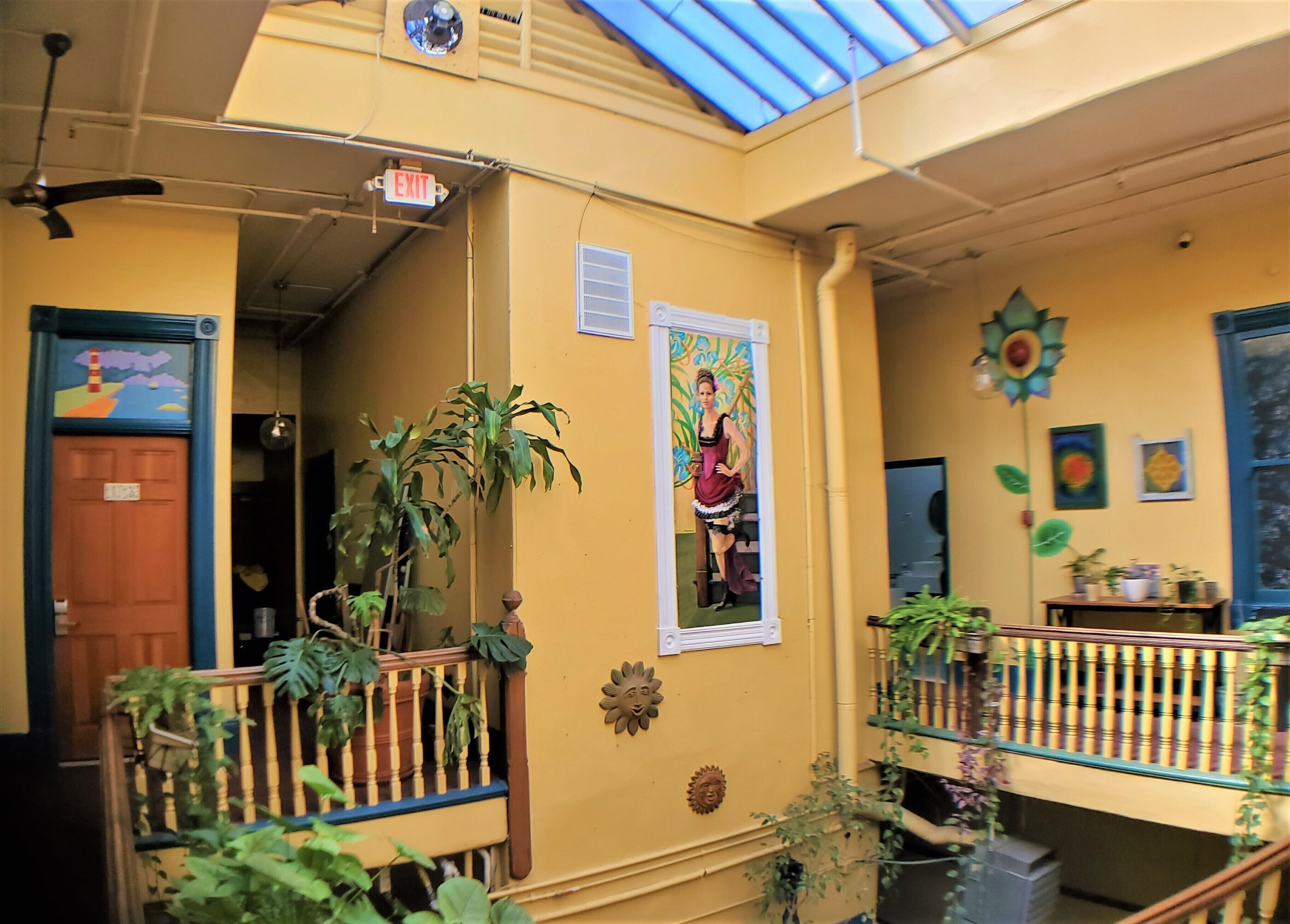 Interior amarelo com ventilador de teto, placa de saída, porta com um mural colorido e uma varanda com plantas.