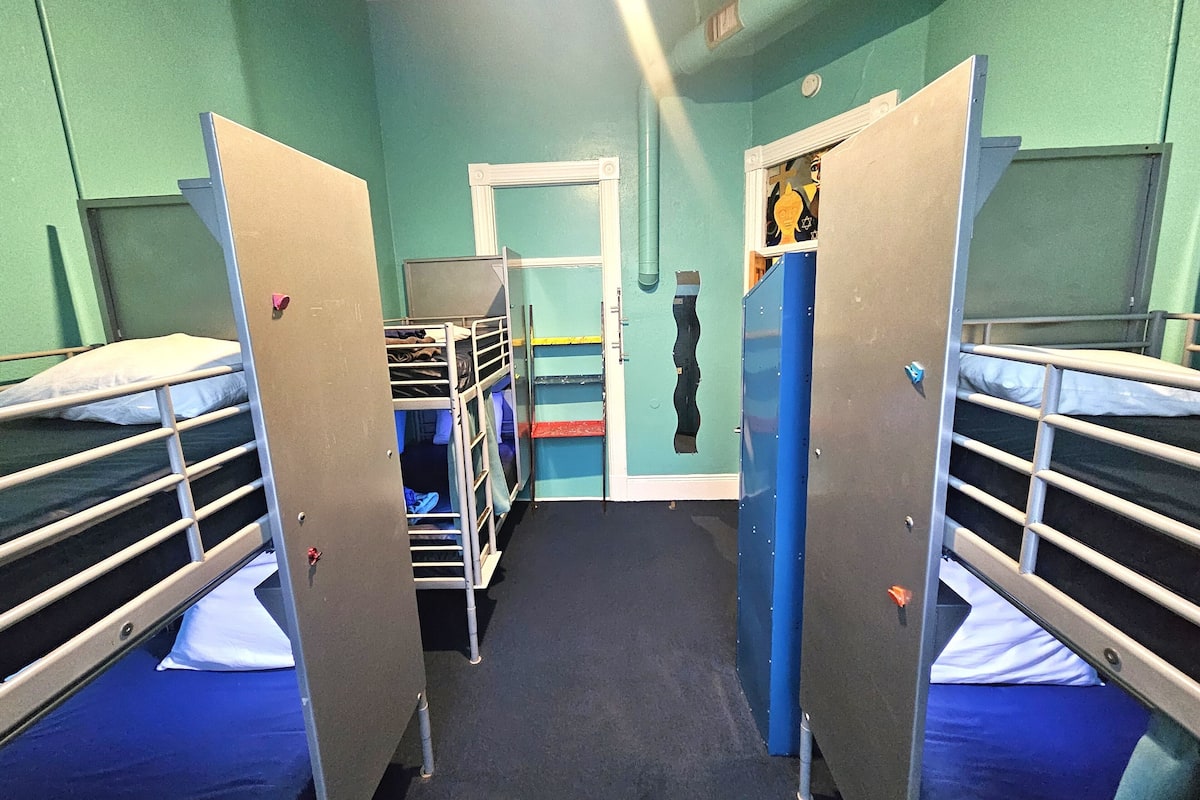 Une chambre de dortoir avec des lits superposés, une porte avec un miroir et une petite étagère où sont posés des objets personnels.