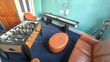 A room with a foosball table, a pool table, and two leather chairs.