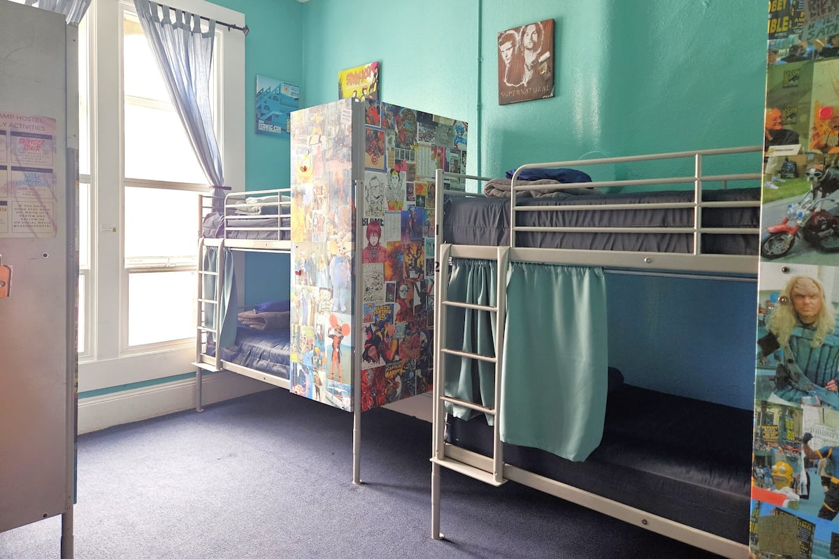 Une chambre de dortoir avec des lits superposés, une fenêtre avec des rideaux et un mur décoré de divers affiches et de bandes dessinées.