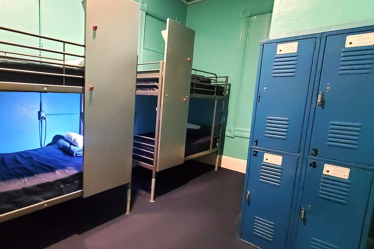 Une chambre de dortoir avec des lits superposés, un bureau et des casiers bleus.
