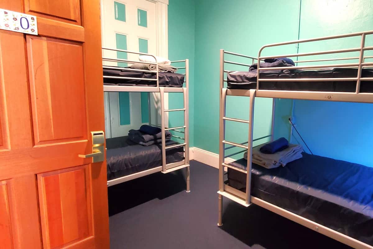 Une chambre de dortoir avec des lits superposés, une porte en bois et des murs de couleur turquoise.