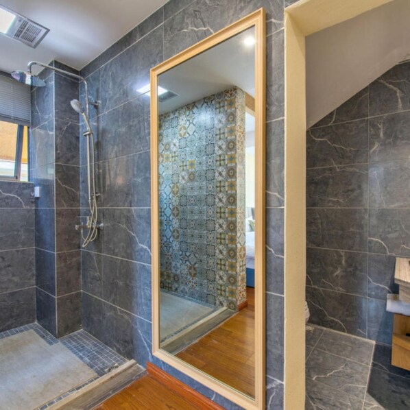 Un baño moderno con baldosas de mármol oscuro, ducha con puerta de cristal y pared de azulejos con diseño.