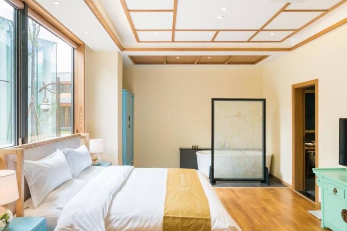 A bedroom with a bed, bedside tables, a window, and a view of the outside.