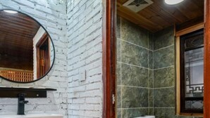 A bathroom with a white brick wall, a round mirror, a white sink, and a toilet. - Floral Hotel · Kuan Tang Lijiang (Lijiang)