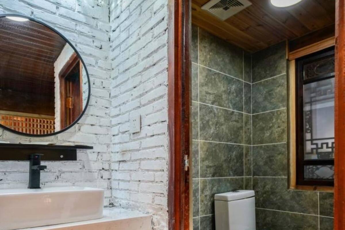 Un baño con pared de ladrillo blanco, un espejo redondo, un lavabo blanco y un inodoro.