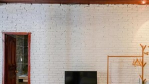 A room with a white brick wall, a wooden desk with a TV, a coat rack, and a door leading to a bathroom. - Floral Hotel · Kuan Tang Lijiang (Lijiang)