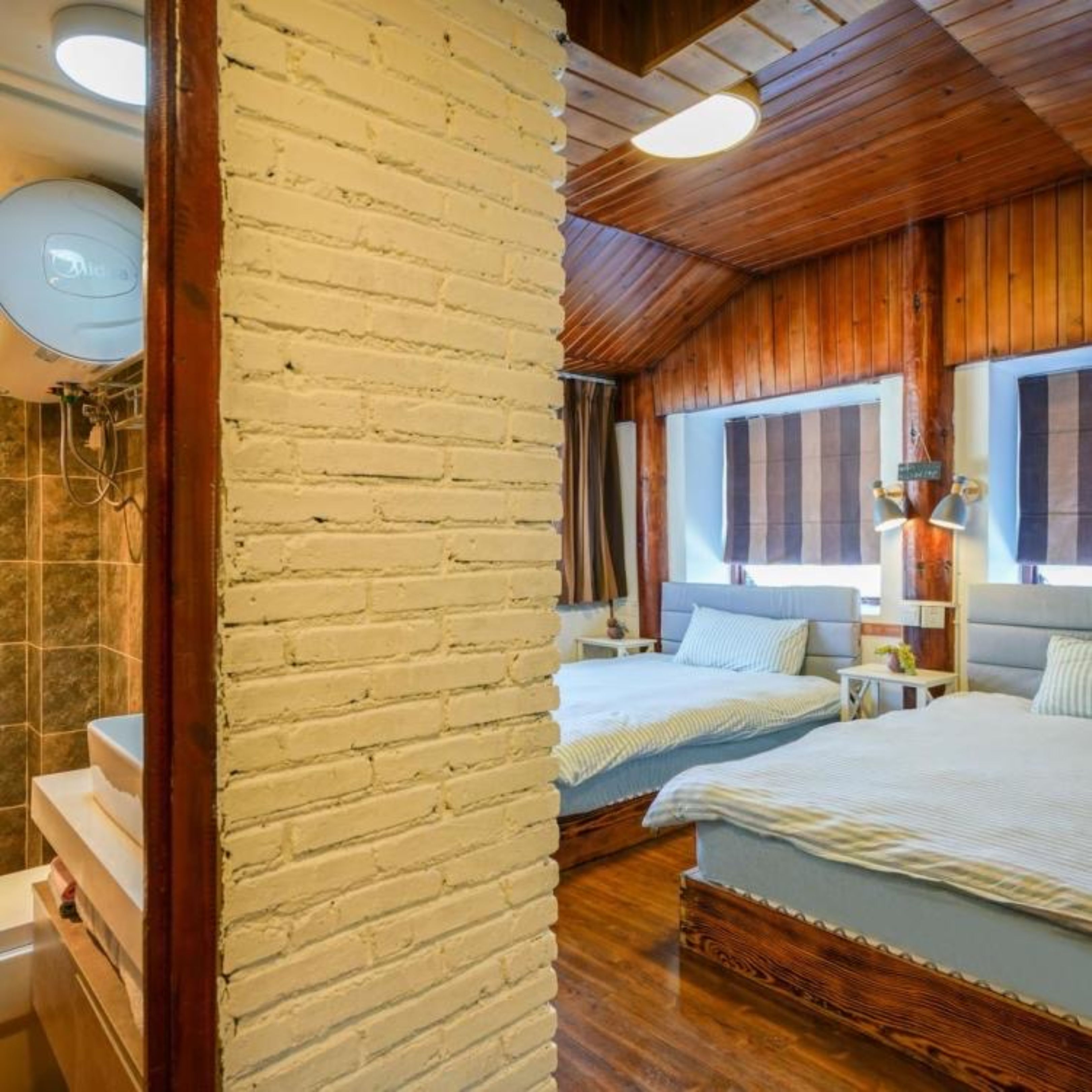 Un dormitorio con dos camas, paredes de madera, un pilar de ladrillo y un baño con ducha.