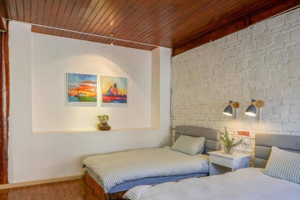 Un dormitorio con dos camas, una pared de ladrillo blanco, techo de madera y dos cuadros en la pared.
