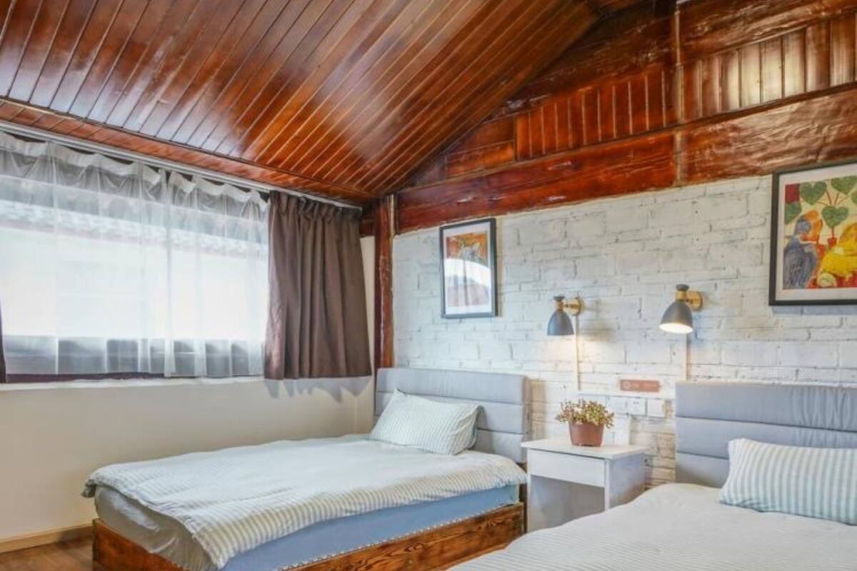 Una habitación con dos camas de madera, una pared de ladrillo blanco y un techo de madera.