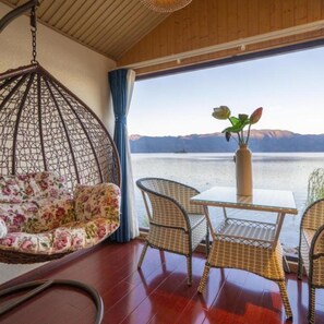 A room with a hanging chair, a floral sofa, wicker chairs, and a table with a vase of flowers.