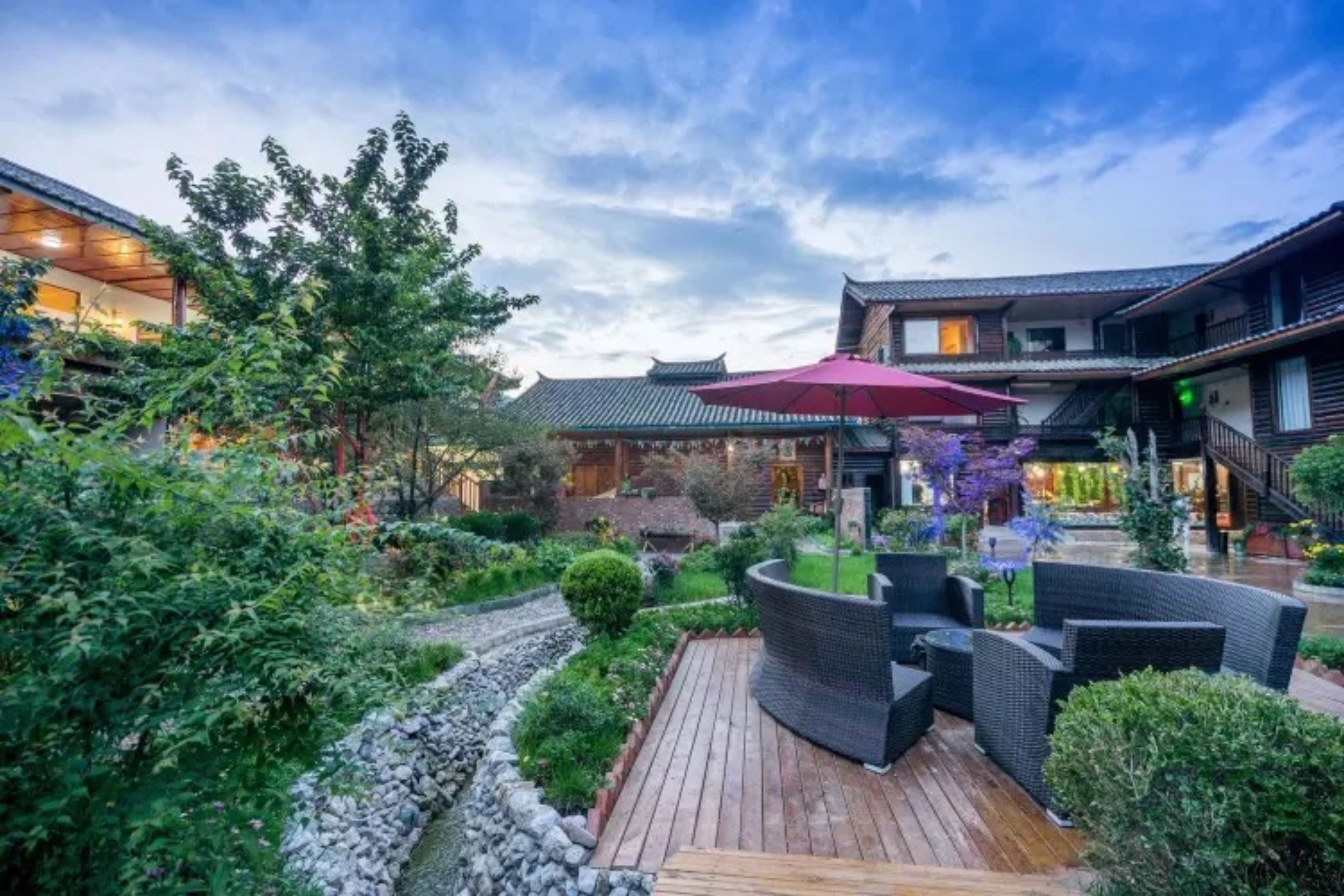 A traditional-style courtyard with wooden flooring, a seating area with wicker furniture, and a red umbrella.