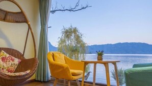 Una habitación con piso de madera, una silla colgante, un sillón amarillo, una pequeña mesa con una planta y vista a un lago y montañas.