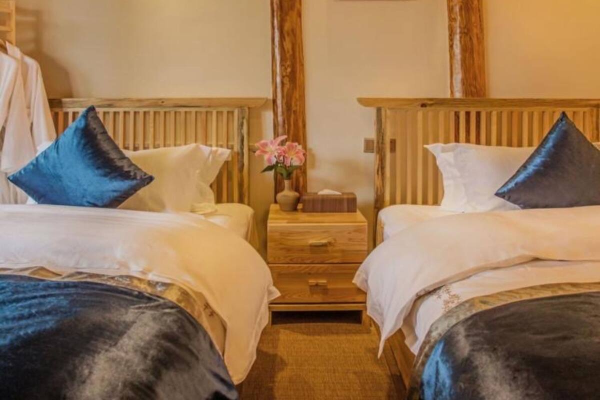 Habitación de hotel con dos camas, cabeceros de madera, una mesita de noche con un florero y un cuadro en la pared.