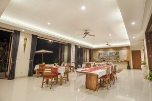 A spacious dining area with multiple tables and chairs, ceiling fans, and a large painting on the wall.