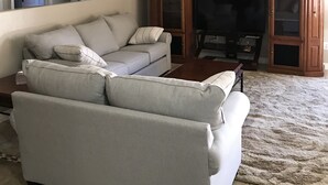 A living room with a grey sectional sofa, a wooden entertainment center, and a flat-screen TV. - Experience Casa Grande charm in our spacious 4-bedroom retreat (Casa Grande)