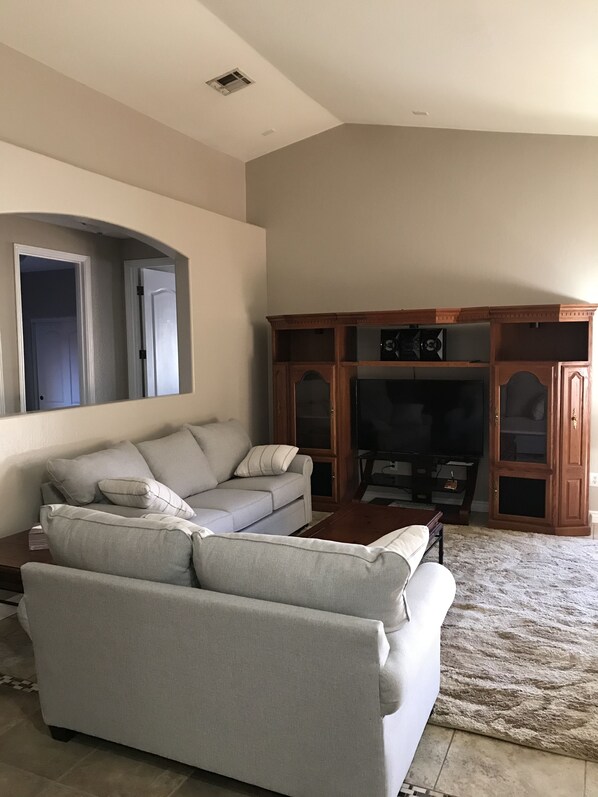 A living room with a grey sectional sofa, a wooden entertainment center, and a flat-screen TV.