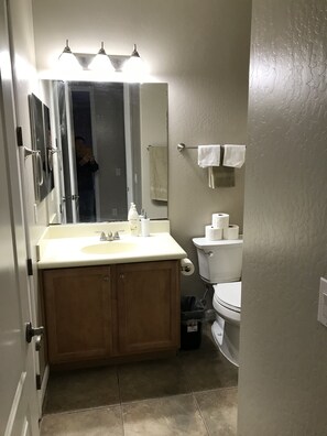 A bathroom with a sink, mirror, towel rack, toilet, and a trash bin.