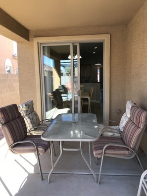 An outdoor patio area with a glass door leading to a kitchen, a table, and two striped sofas.