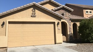 A residential house with a beige garage door, a stone facade, and a clear blue sky. - Experience Casa Grande charm in our spacious 4-bedroom retreat (Casa Grande)