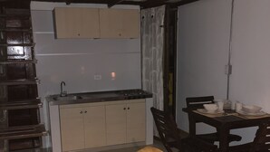 Et lille køkken med gasblus, vask og spiseplads med bænk og stole.