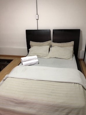 Un letto con una testiera nera, cuscini beige e una coperta bianca.