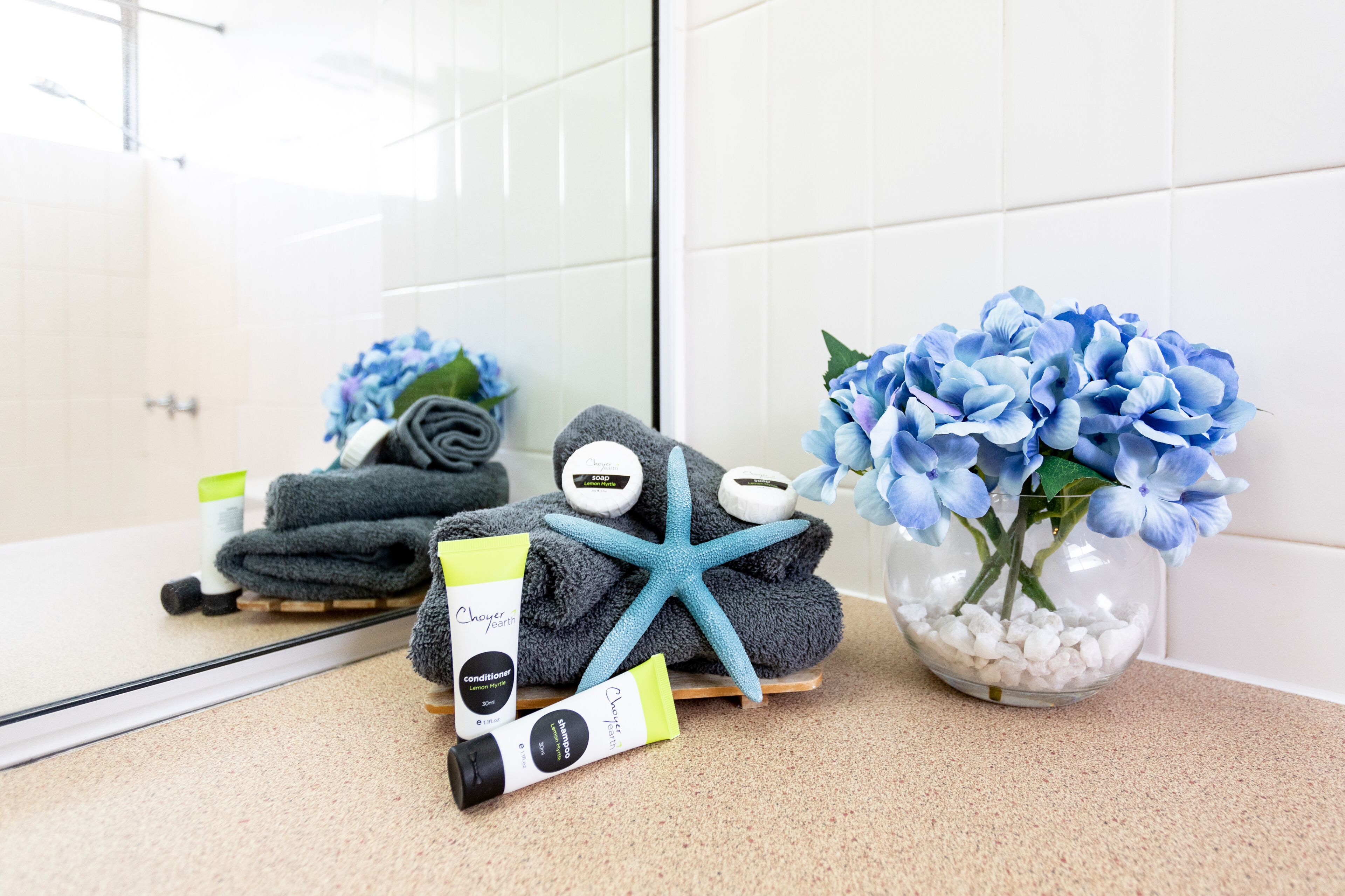 Et badeværelse med spejl, toiletartikler, håndklæder og en blomstervase.